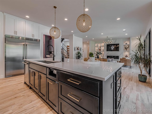 kitchen with light stone counters, pendant lighting, a center island with sink, white cabinetry, and built in refrigerator