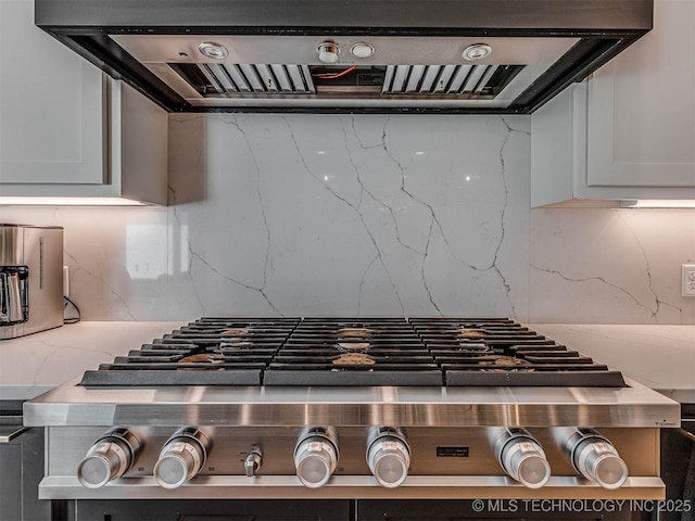 interior details with white cabinets, tasteful backsplash, stainless steel gas cooktop, and range hood