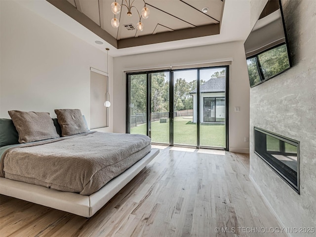 unfurnished bedroom featuring access to outside, a tray ceiling, light hardwood / wood-style floors, and a notable chandelier