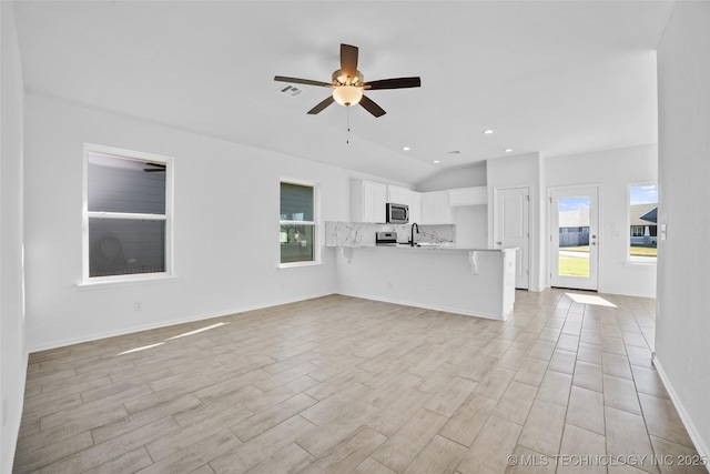 unfurnished living room featuring ceiling fan, sink, light hardwood / wood-style floors, and vaulted ceiling