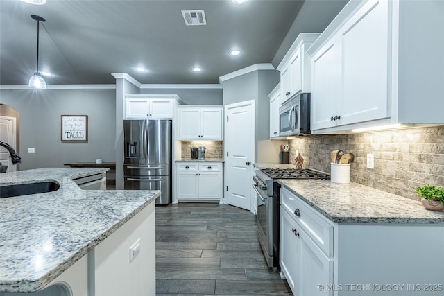 kitchen with appliances with stainless steel finishes, pendant lighting, white cabinets, light stone counters, and sink