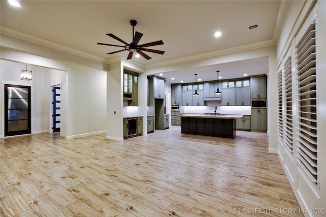 kitchen with pendant lighting, ornamental molding, a kitchen island with sink, and light hardwood / wood-style flooring