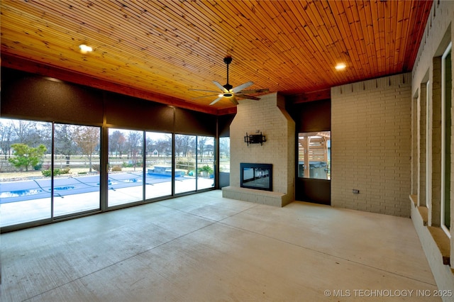 unfurnished sunroom featuring ceiling fan, a large fireplace, and wood ceiling