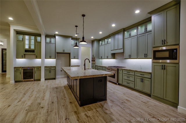 kitchen with green cabinets, wine cooler, pendant lighting, a kitchen island with sink, and appliances with stainless steel finishes