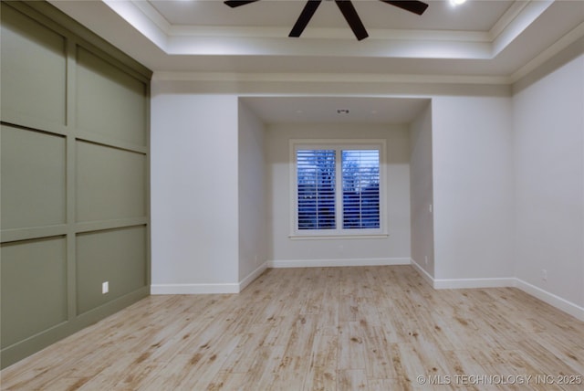 empty room with ceiling fan, light wood-type flooring, ornamental molding, and a tray ceiling