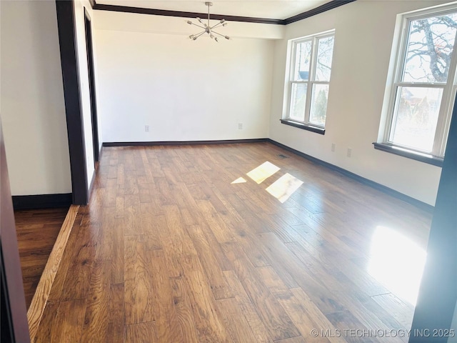 spare room featuring hardwood / wood-style flooring, crown molding, an inviting chandelier, and a wealth of natural light