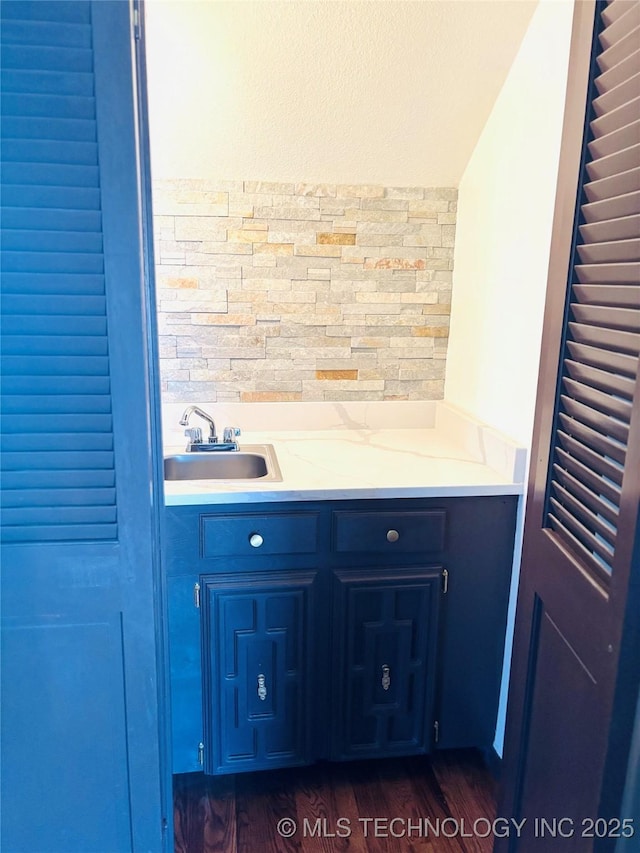 bar with sink, backsplash, dark hardwood / wood-style floors, light stone counters, and blue cabinets