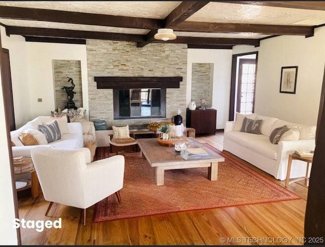 living room with hardwood / wood-style flooring, a stone fireplace, and beamed ceiling