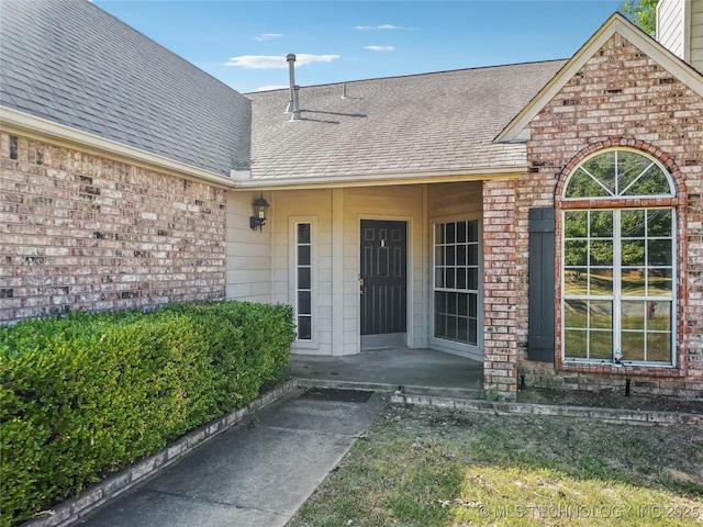 doorway to property with a porch, brick siding, and roof with shingles