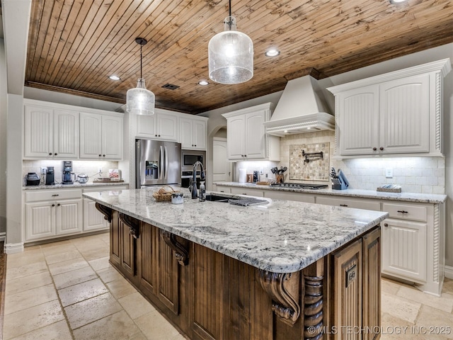 kitchen with stainless steel appliances, an island with sink, premium range hood, and white cabinetry