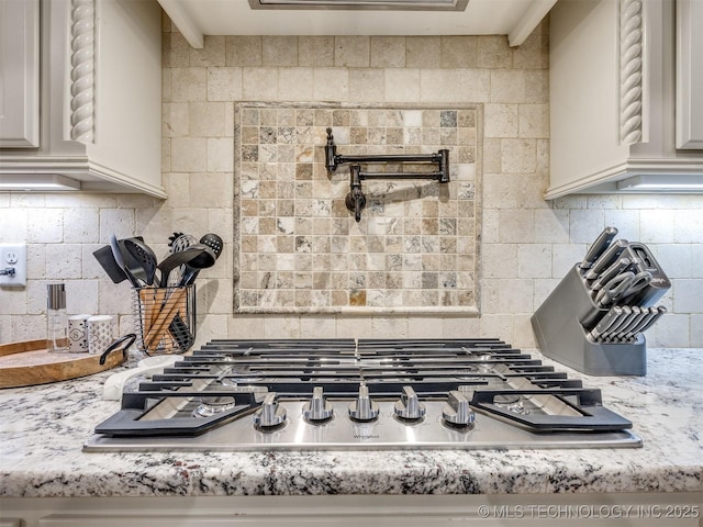 details featuring stainless steel gas stovetop, light stone countertops, and backsplash