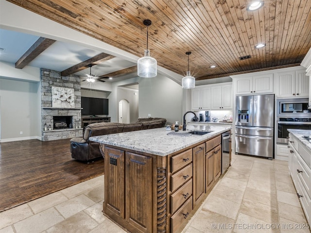 kitchen featuring white cabinetry, a stone fireplace, appliances with stainless steel finishes, and a center island with sink