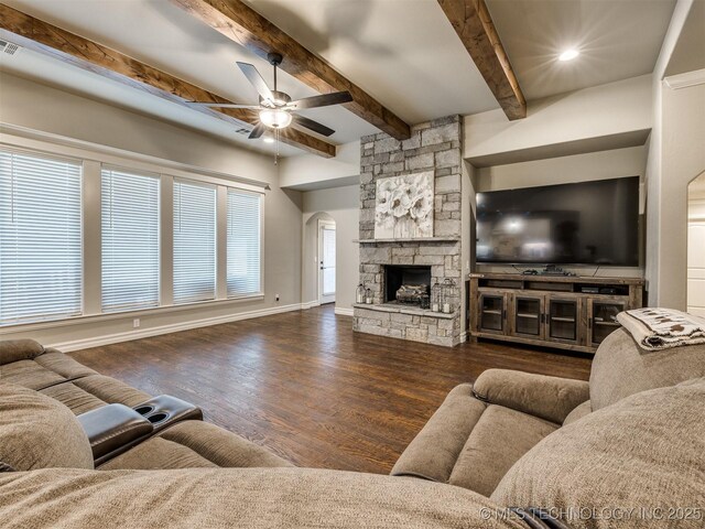 living room with dark wood-type flooring, ceiling fan, a stone fireplace, and beam ceiling