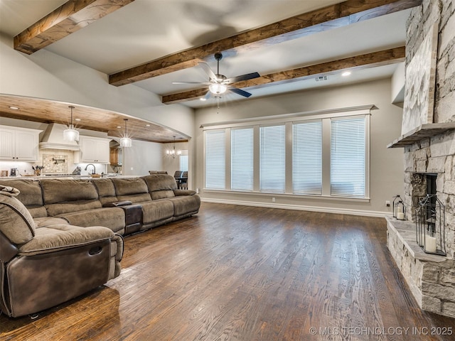 living room with dark wood-type flooring, beam ceiling, a healthy amount of sunlight, a fireplace, and ceiling fan with notable chandelier