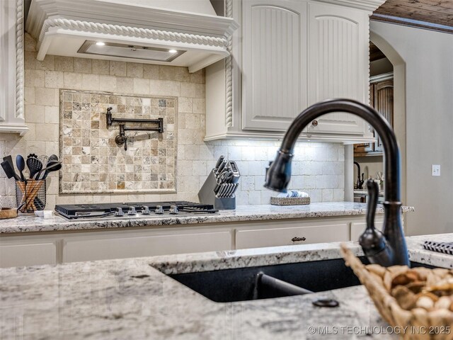 kitchen featuring backsplash, light stone countertops, sink, and white cabinets