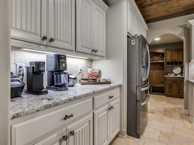 kitchen with white cabinetry, stainless steel fridge, decorative backsplash, light stone counters, and wooden ceiling