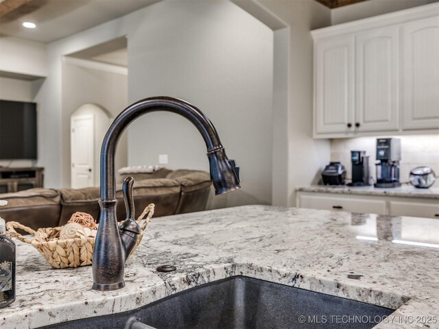 room details featuring white cabinetry, light stone countertops, sink, and backsplash