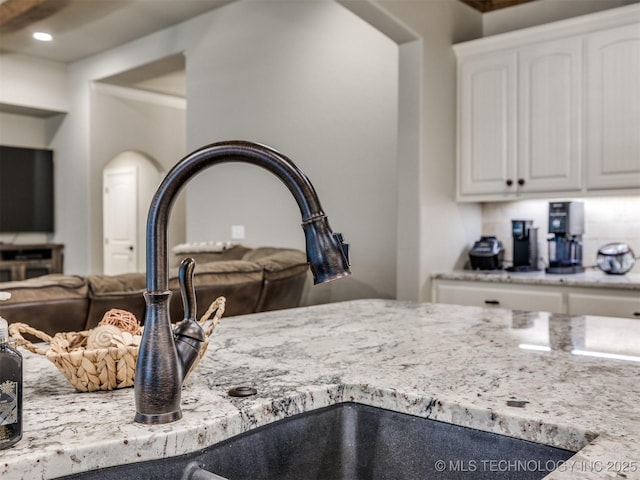 interior details with light stone counters, a sink, and white cabinetry