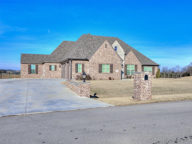 french country inspired facade with brick siding, driveway, a shingled roof, and a front lawn