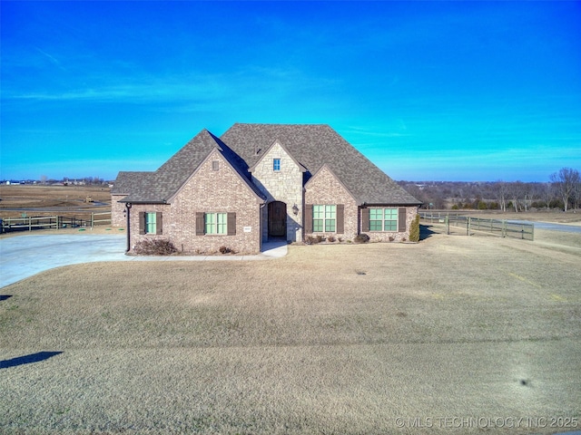 french provincial home with brick siding, stone siding, a shingled roof, and fence