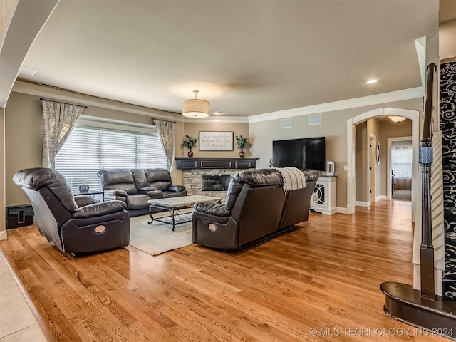 living room featuring plenty of natural light, a stone fireplace, ornamental molding, and light hardwood / wood-style flooring