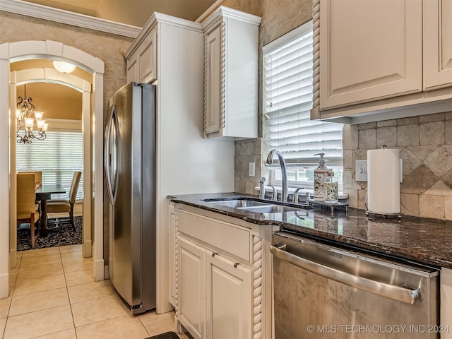 kitchen featuring sink, an inviting chandelier, stainless steel appliances, light tile patterned floors, and dark stone counters