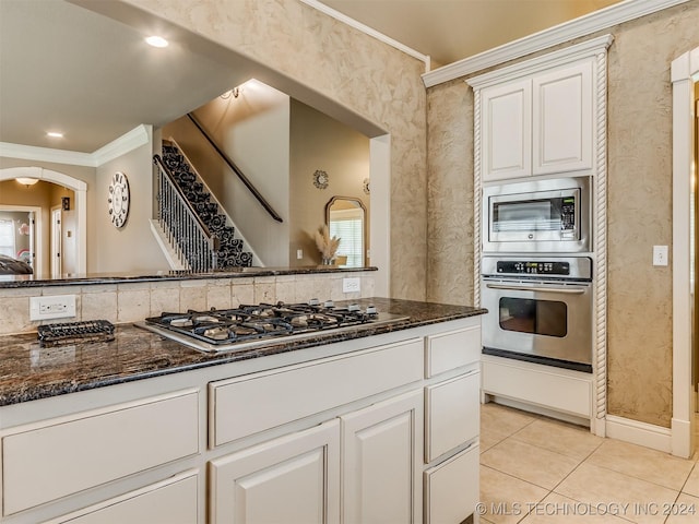 kitchen with appliances with stainless steel finishes, white cabinetry, dark stone countertops, ornamental molding, and light tile patterned floors