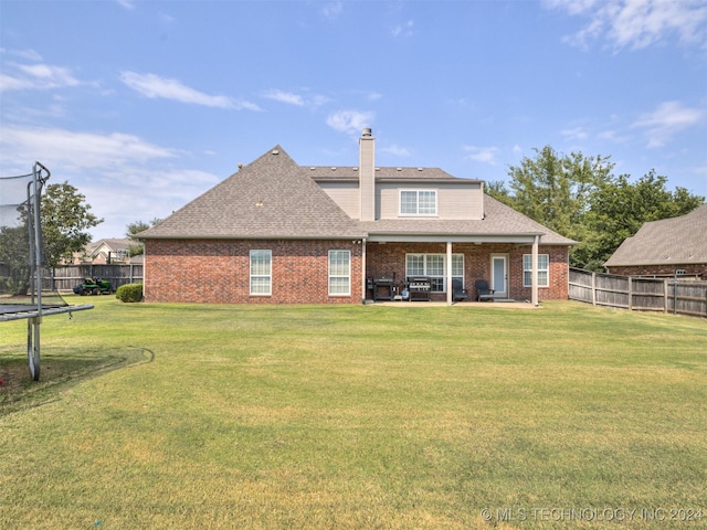 rear view of house featuring a lawn, a trampoline, and a patio area