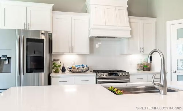 kitchen with white cabinetry, custom range hood, and appliances with stainless steel finishes