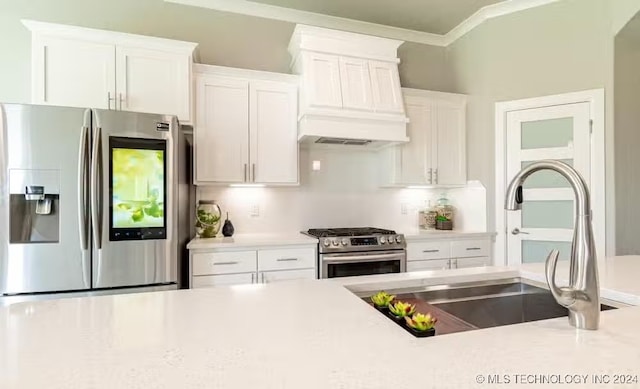 kitchen with sink, appliances with stainless steel finishes, white cabinets, custom range hood, and ornamental molding