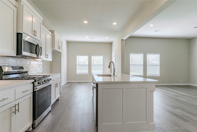 kitchen featuring appliances with stainless steel finishes, backsplash, sink, a center island with sink, and white cabinets