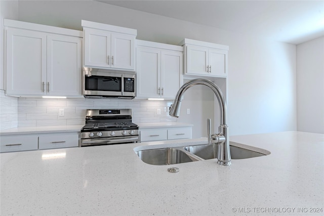 kitchen with white cabinets, stainless steel appliances, light stone countertops, and sink