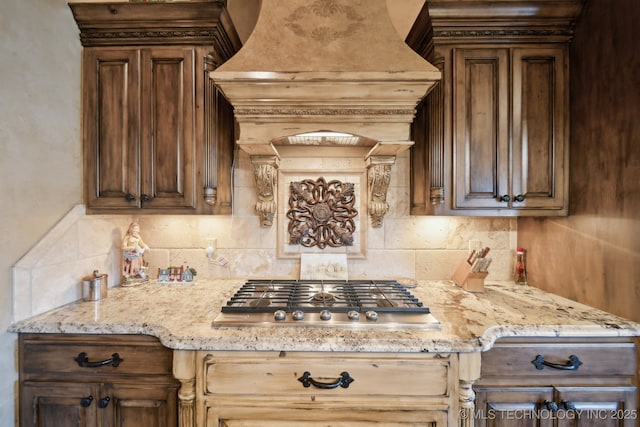 kitchen with tasteful backsplash, premium range hood, stainless steel gas cooktop, and light stone counters