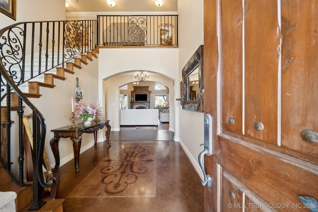 foyer entrance featuring finished concrete floors, stairway, baseboards, arched walkways, and a towering ceiling