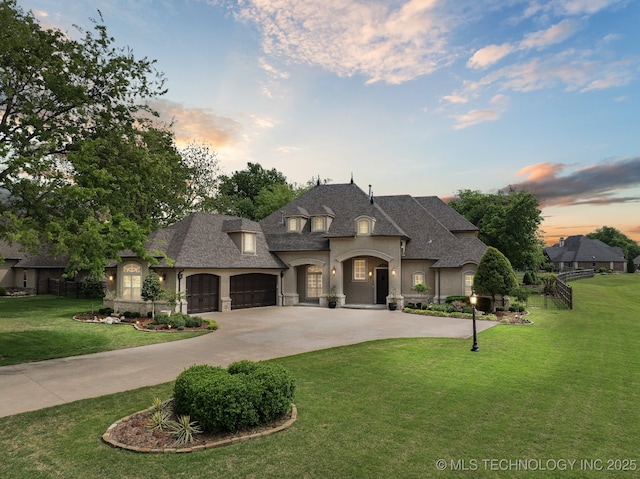 french country home with a garage, a shingled roof, a yard, stucco siding, and curved driveway