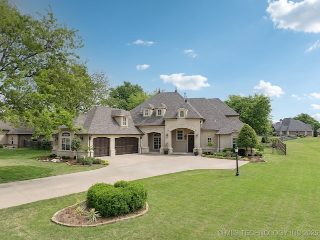 french country style house with a shingled roof, a front yard, an attached garage, curved driveway, and stucco siding