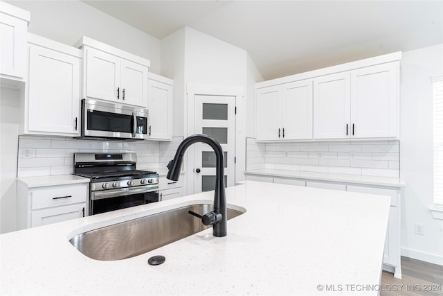 kitchen featuring light stone countertops, decorative backsplash, white cabinets, and stainless steel appliances