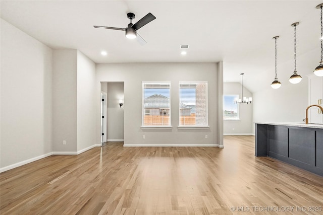 unfurnished living room with ceiling fan with notable chandelier, light hardwood / wood-style flooring, vaulted ceiling, and sink