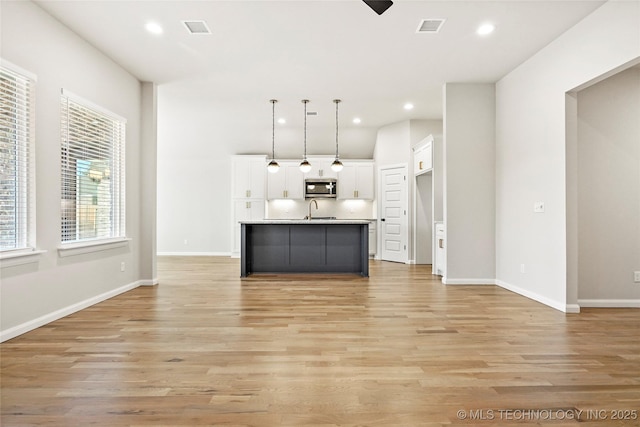 kitchen featuring white cabinetry, sink, pendant lighting, light hardwood / wood-style floors, and a center island with sink