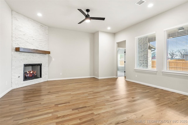 unfurnished living room featuring ceiling fan, a stone fireplace, and light wood-type flooring