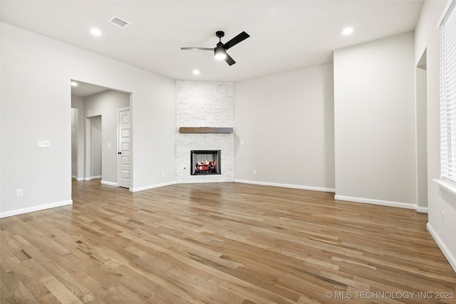 unfurnished living room with ceiling fan, a stone fireplace, and light hardwood / wood-style flooring