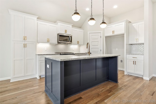 kitchen featuring tasteful backsplash, an island with sink, white cabinets, and pendant lighting