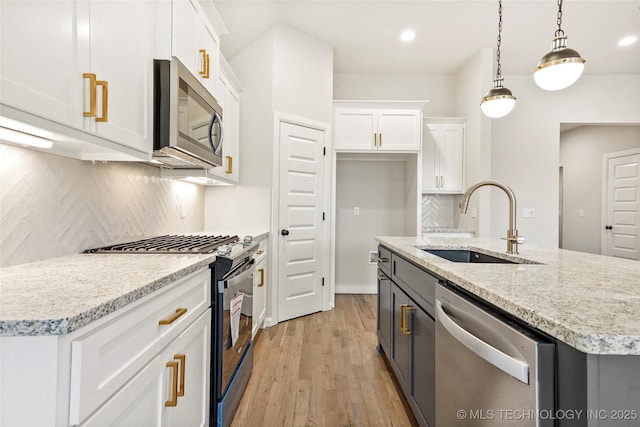 kitchen featuring stainless steel appliances, a kitchen island with sink, sink, white cabinets, and hanging light fixtures