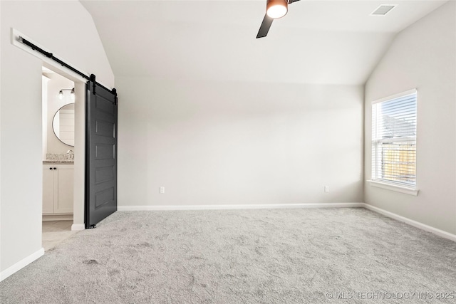 unfurnished bedroom featuring ensuite bathroom, light colored carpet, ceiling fan, a barn door, and lofted ceiling