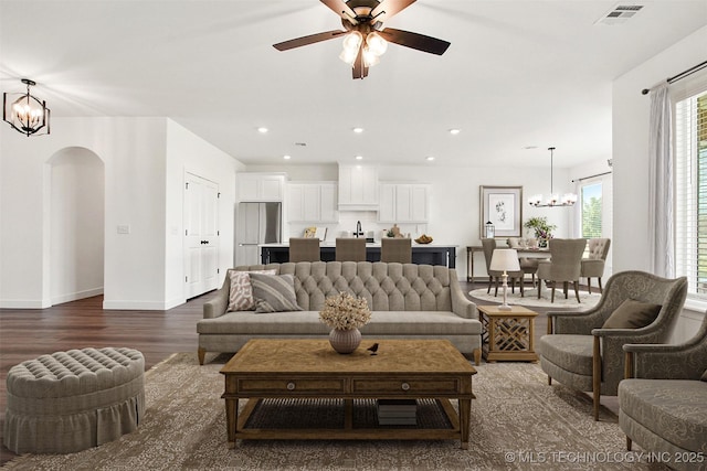 living room with ceiling fan with notable chandelier and dark hardwood / wood-style flooring