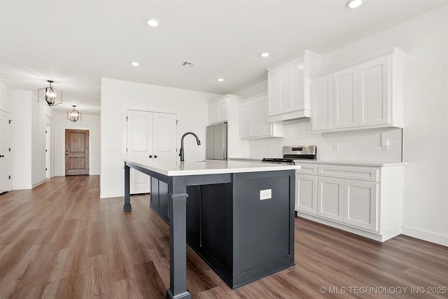 kitchen featuring white cabinets, stainless steel gas stove, and a kitchen island with sink