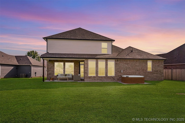 back house at dusk with outdoor lounge area, central AC, a yard, and a hot tub