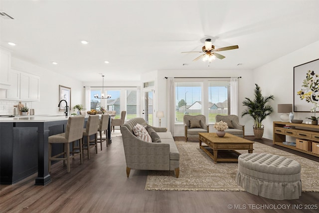 living room with ceiling fan with notable chandelier, sink, dark wood-type flooring, and a wealth of natural light