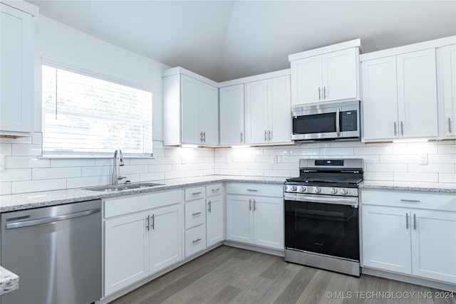 kitchen featuring light stone countertops, white cabinetry, sink, stainless steel appliances, and vaulted ceiling