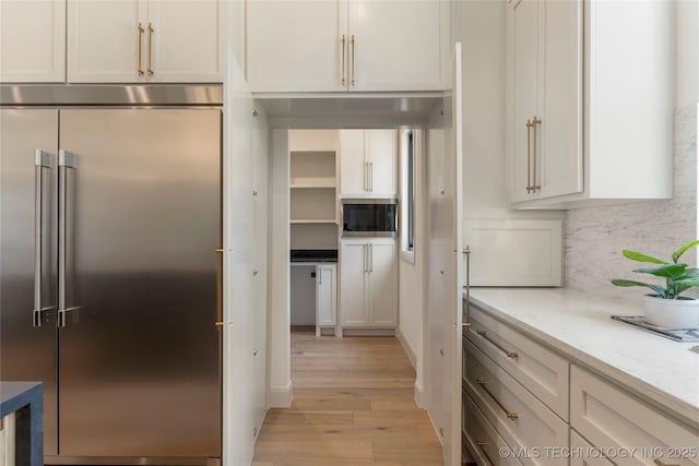 kitchen with white cabinets, built in appliances, decorative backsplash, light wood-type flooring, and light stone counters